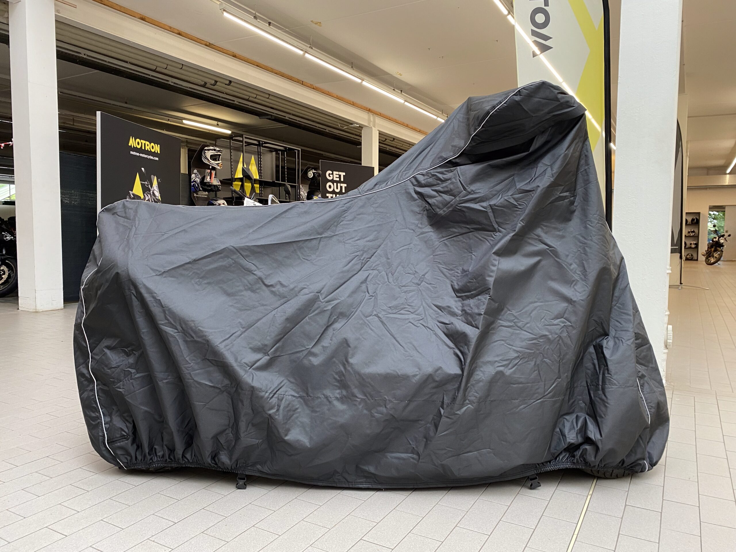 Yamaha T Max in the showroom, Scooter completely covered with a motorcycle cover, calm background.